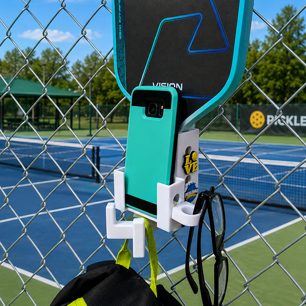Paddle Mate in white mounted on a fence with Crocs Jibbitz charms, phone caddy attachment and eyeglasses ring attached.