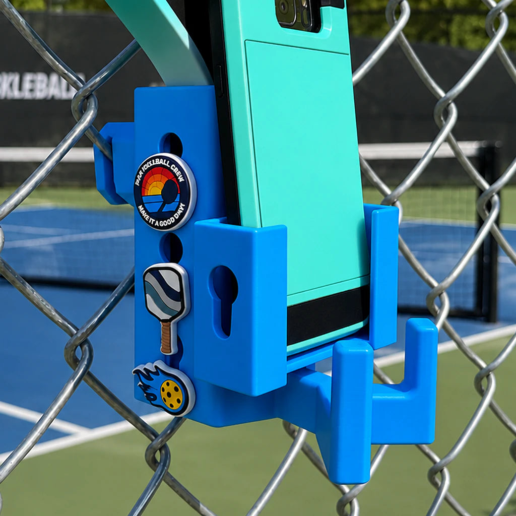Paddle Mate in white mounted on a fence with Crocs Jibbitz charms, phone caddy attachment and eyeglasses ring attached.
